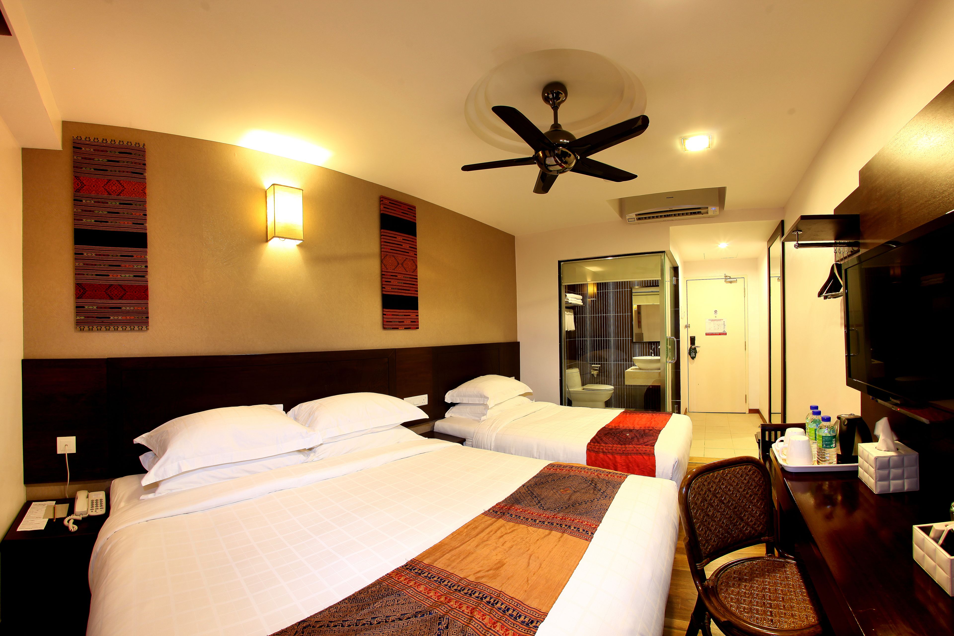 A hotel room with two beds, a ceiling fan, a TV, and a desk with a chair.