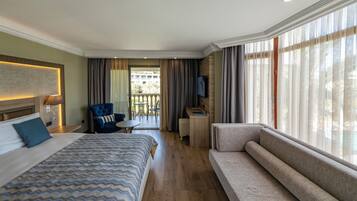 Une chambre d’hôtel avec un lit, un canapé, une télévision, un bureau et un balcon avec des rideaux.