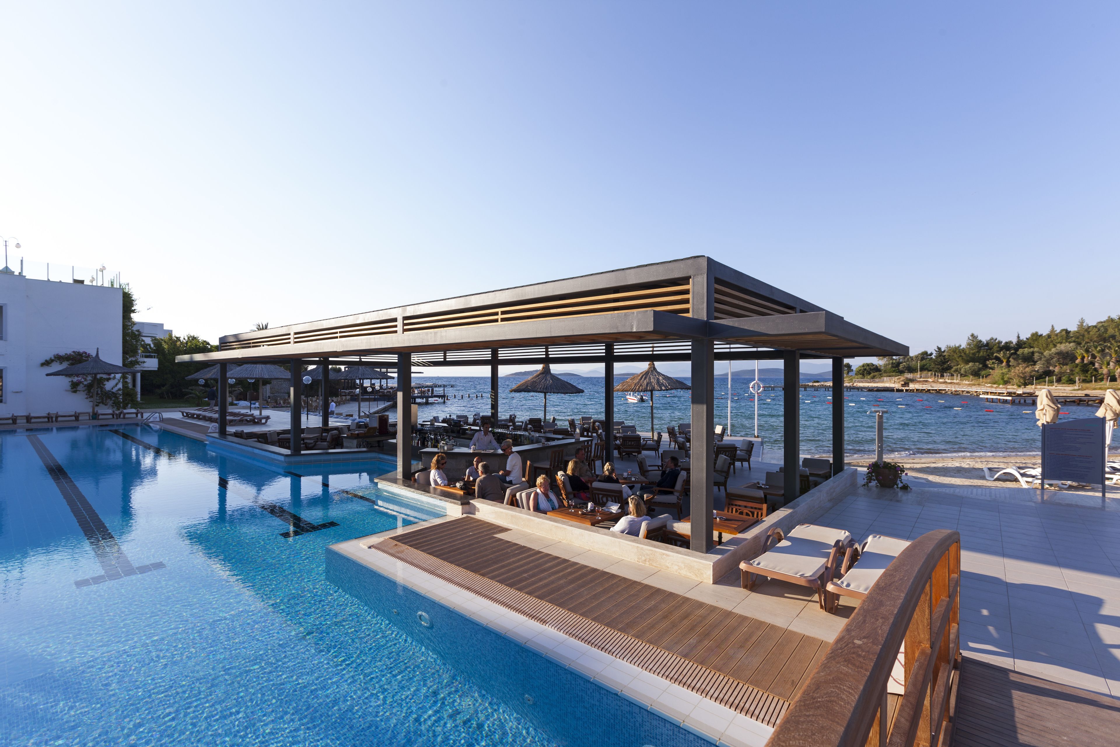 A poolside area with a covered seating area, lounge chairs, and a view of the sea.