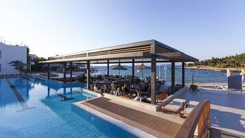 A poolside area with a covered seating area, lounge chairs, and a view of the sea.