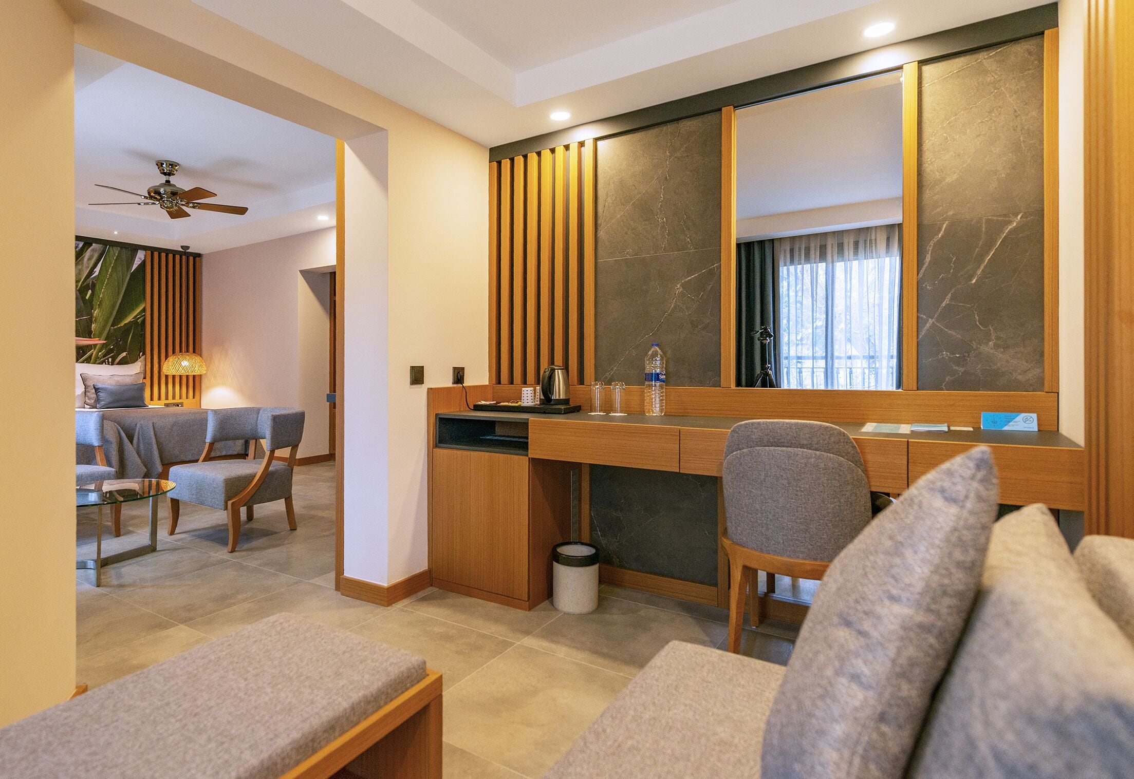 Una habitación de hotel moderna con un escritorio de madera, un sofá cómodo, una zona de comedor y un espejo grande.
