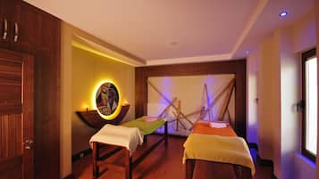 A spa room with two wooden beds, a wall-mounted massage table, and a decorative wall with a circular light fixture.