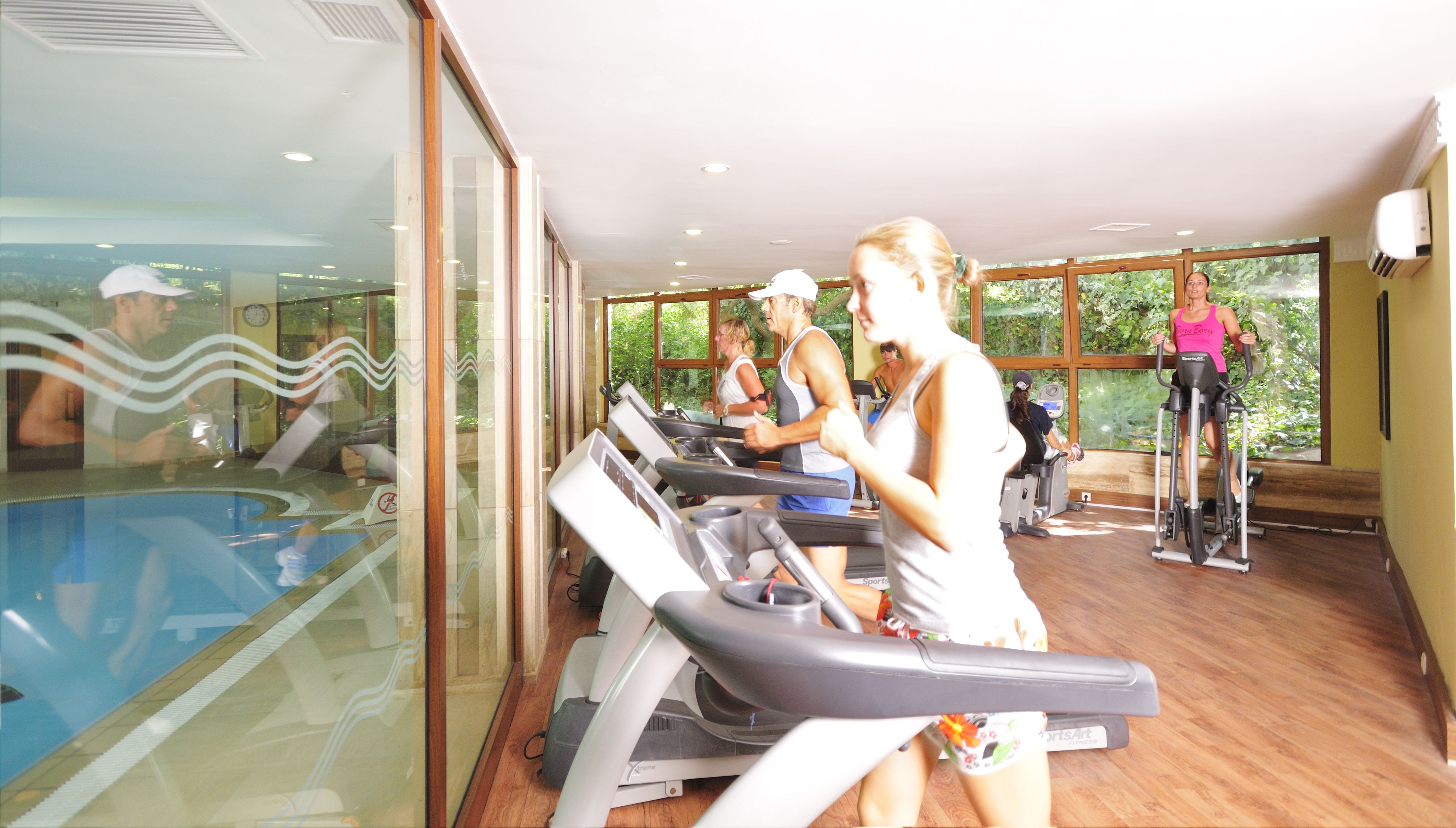 Een fitnessruimte met loopbanden, een zwembad en grote ramen.