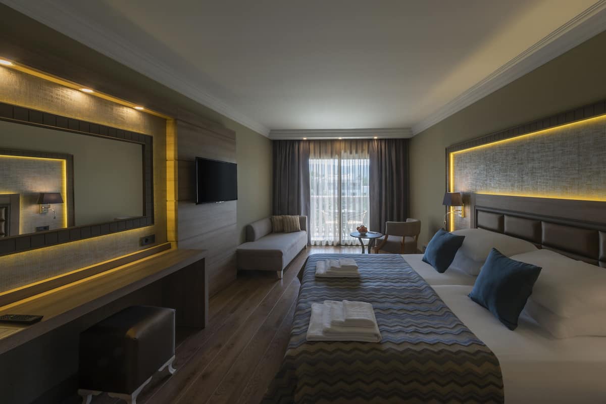 A modern hotel room with a large bed, a sofa, a desk, and a TV.