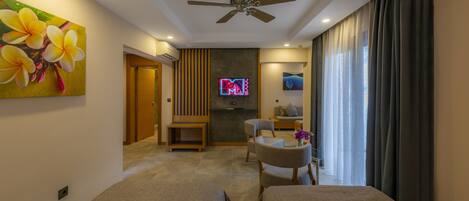 A modern living room with a ceiling fan, a flat-screen TV mounted on a dark wall, a sofa, a coffee table, and a large window with curtains.