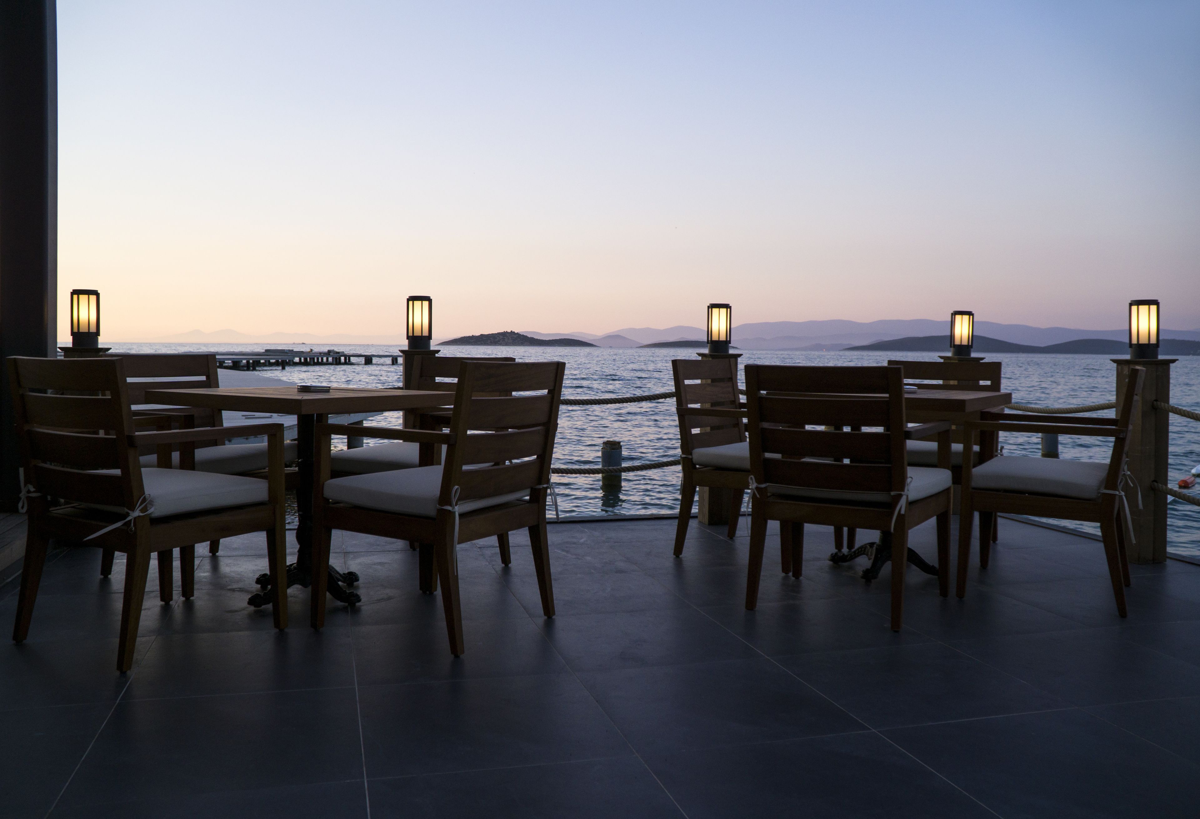 Eine Terrasse mit Holztischen und -stühlen mit Blick auf ein Gewässer und entfernte Inseln.
