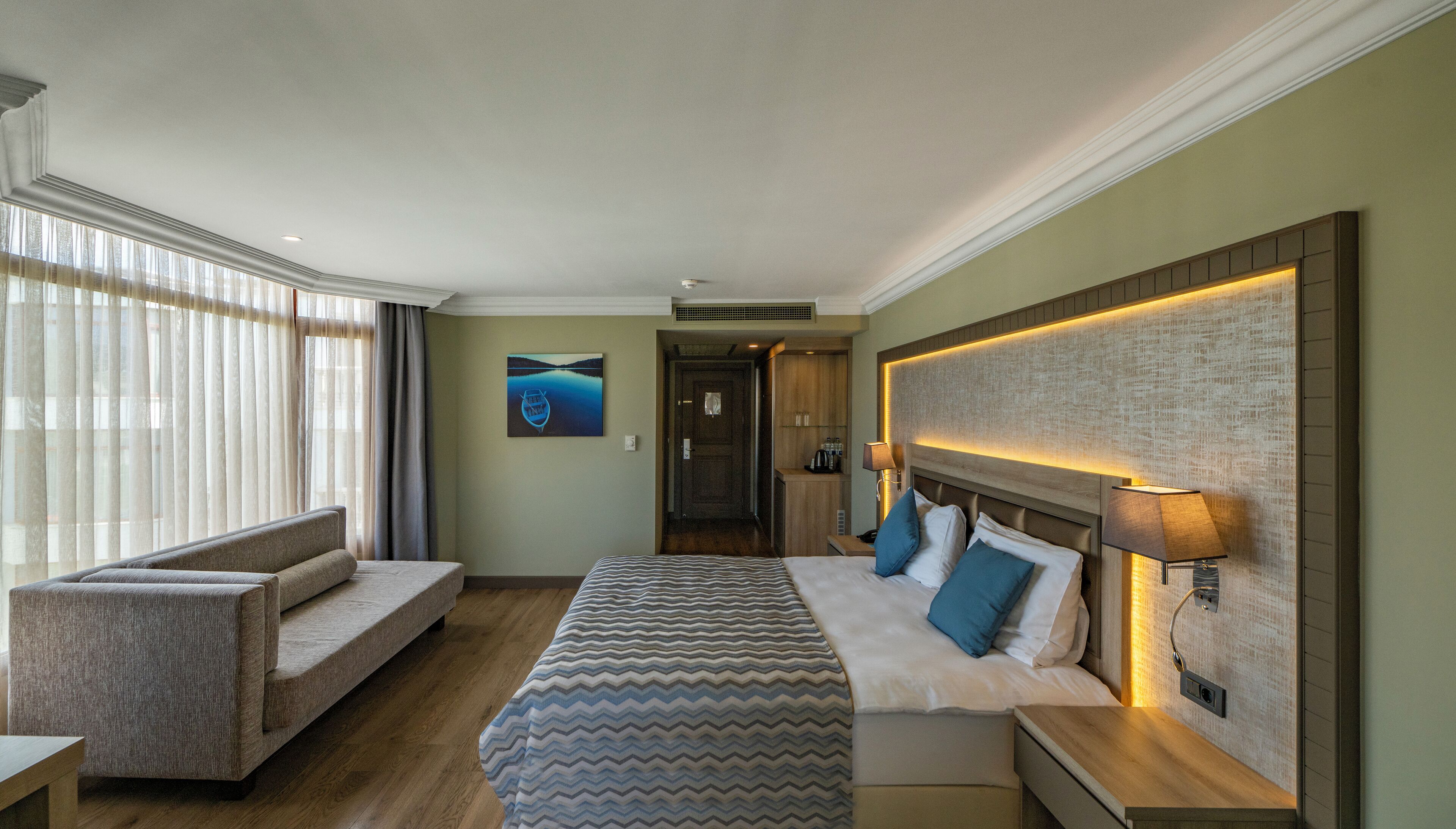 Een hotelkamer met een bed, een sofa, een bureau en uitzicht op de omgeving.