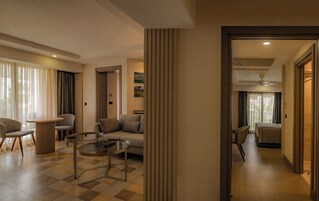 Una habitación de hotel moderna con un sofá, sillones, una mesa de centro de vidrio y vistas al exterior.