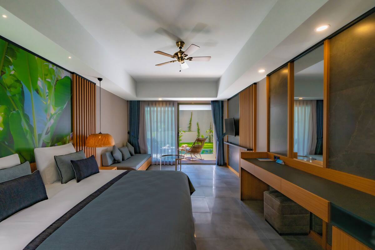 A modern hotel room with a large bed, a seating area, a TV, and a balcony with a view.