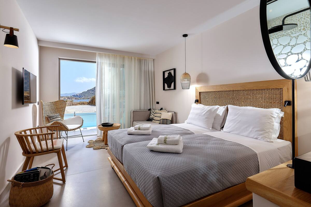 A modern hotel room with two beds, a large window with a view, a TV, and a wicker chair.