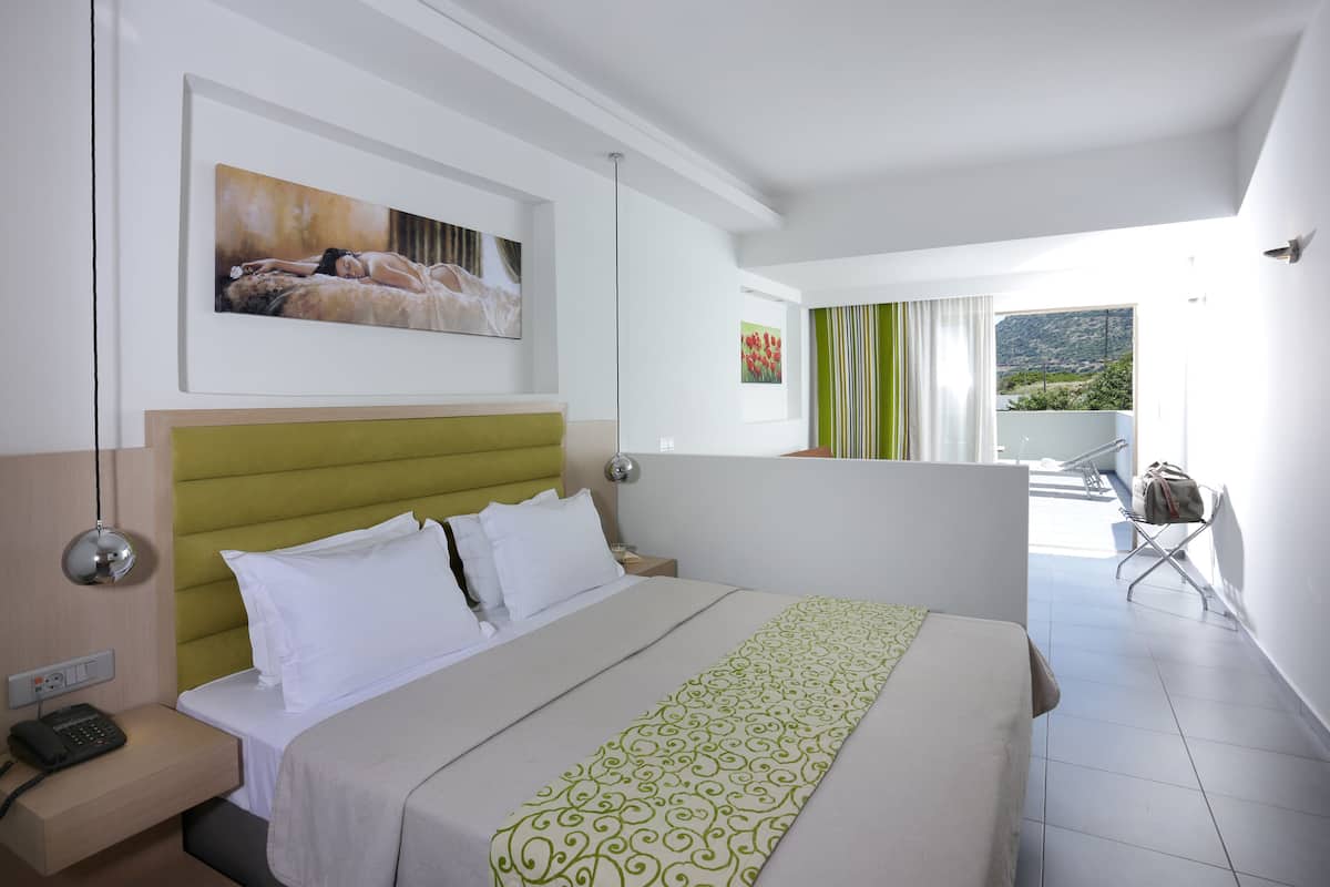 A hotel room with a bed, a nightstand, a telephone, a framed painting, and a view of the outdoors.