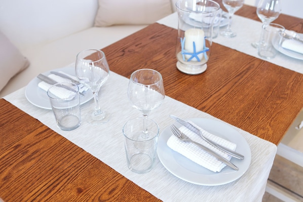 A neatly set dining table with clear glassware, white plates, and silverware, a candle with a blue star decoration, and a white napkin. - La Maison Blanche (Mykonos)