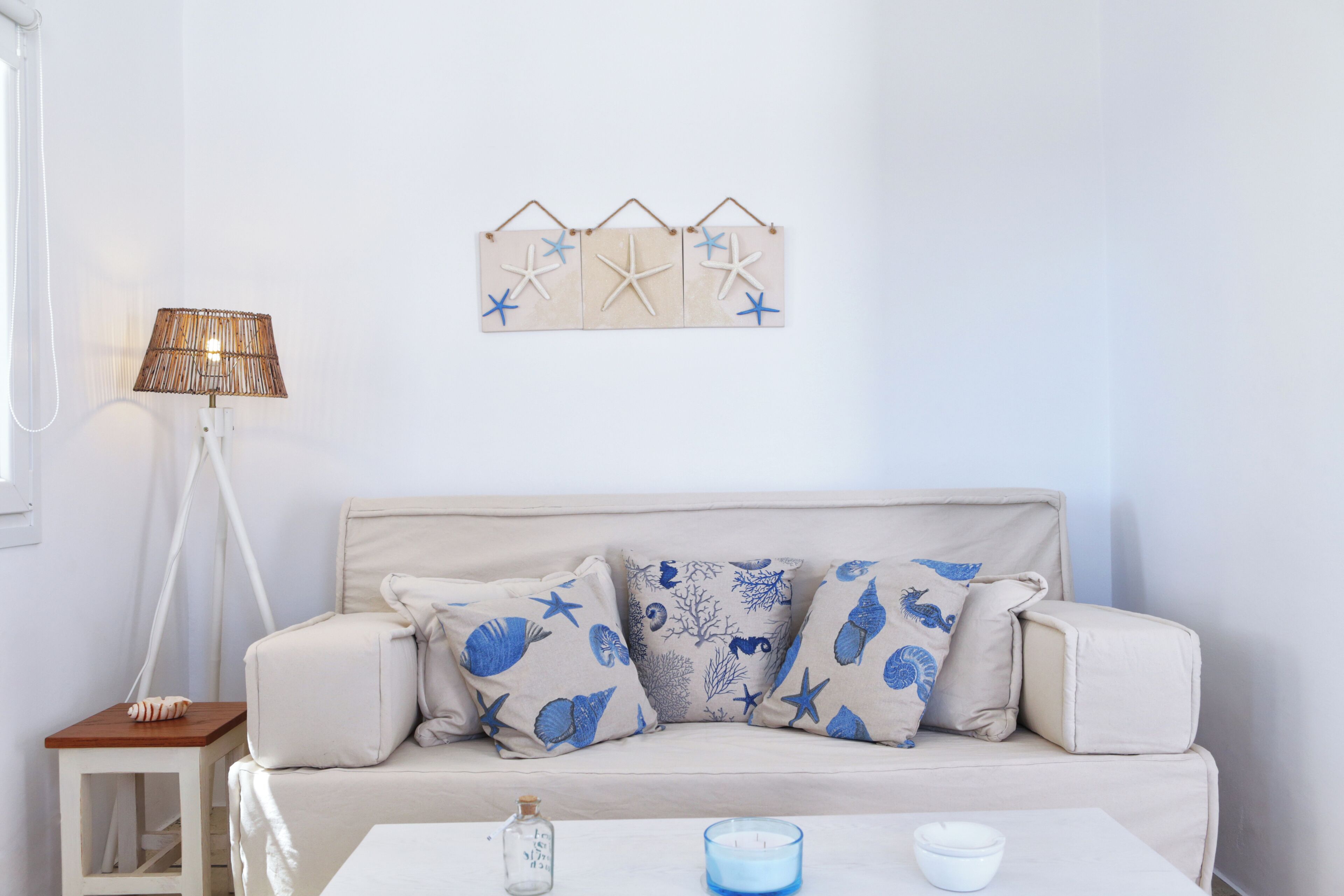 A room with a beige sofa, patterned cushions, a small side table, a floor lamp, and a wall decoration.