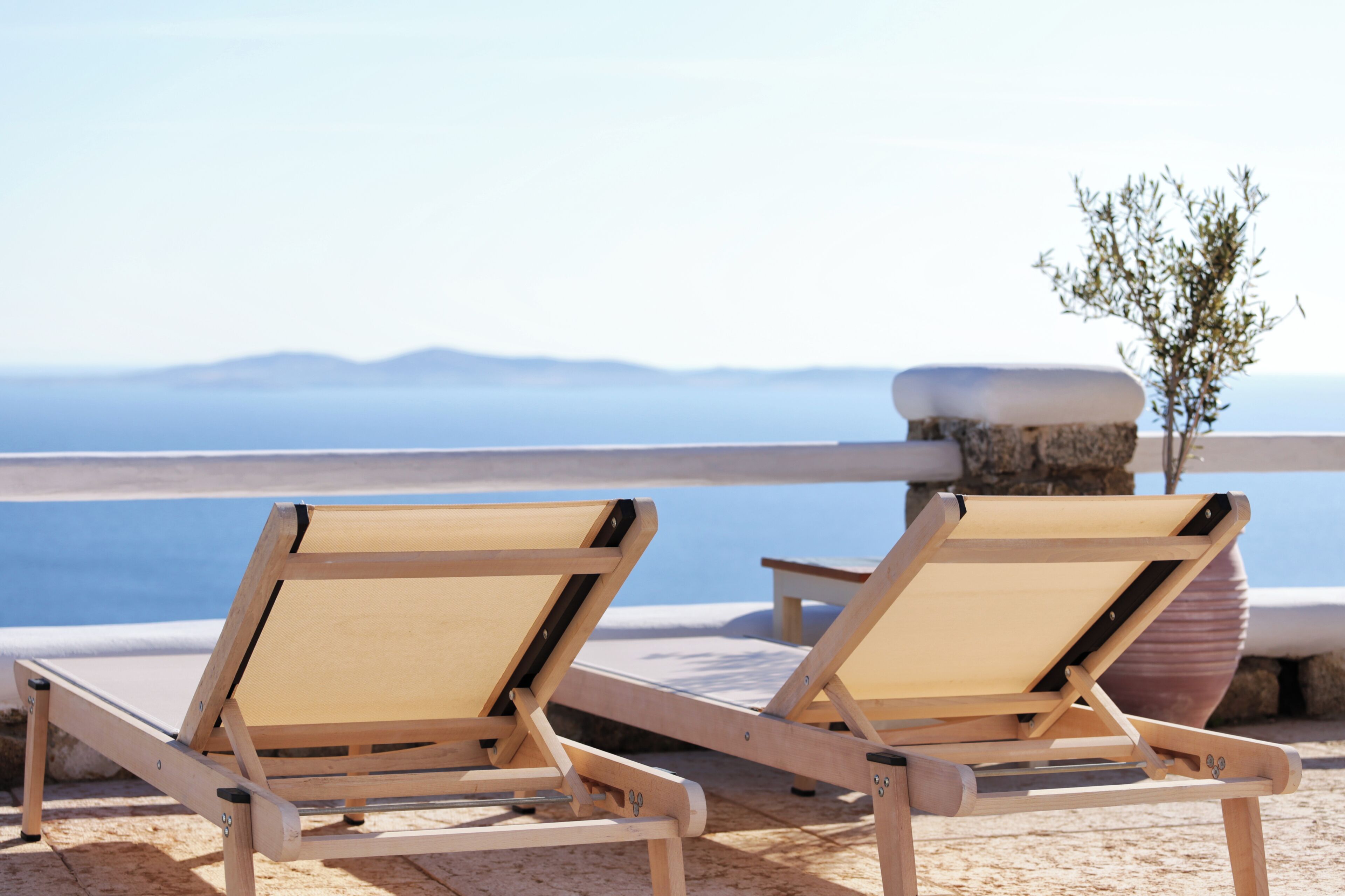 Two wooden lounge chairs with a view of the sea and mountains in the background.