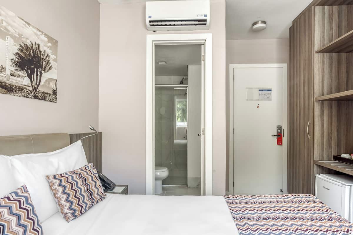 Ein Hotelzimmer mit Bett, Nachttisch, Telefon, einer Tür zum Badezimmer und einem Regal mit Gegenständen.