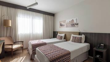 A hotel room with two beds, a desk, a chair, a lamp, and a phone on a nightstand.