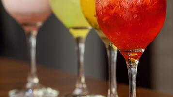 Quatro copos de cocktails com canudos e enfeites de cores diferentes sobre uma superfície de madeira.