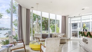 Habitación de hotel moderna con ventanas grandes, un pouf amarillo y vista a un cuerpo de agua.