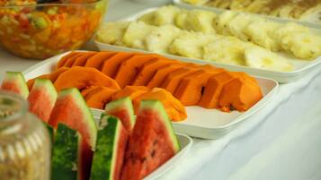 Un bufé con diversos platos, incluyendo frutas y verduras cortadas.