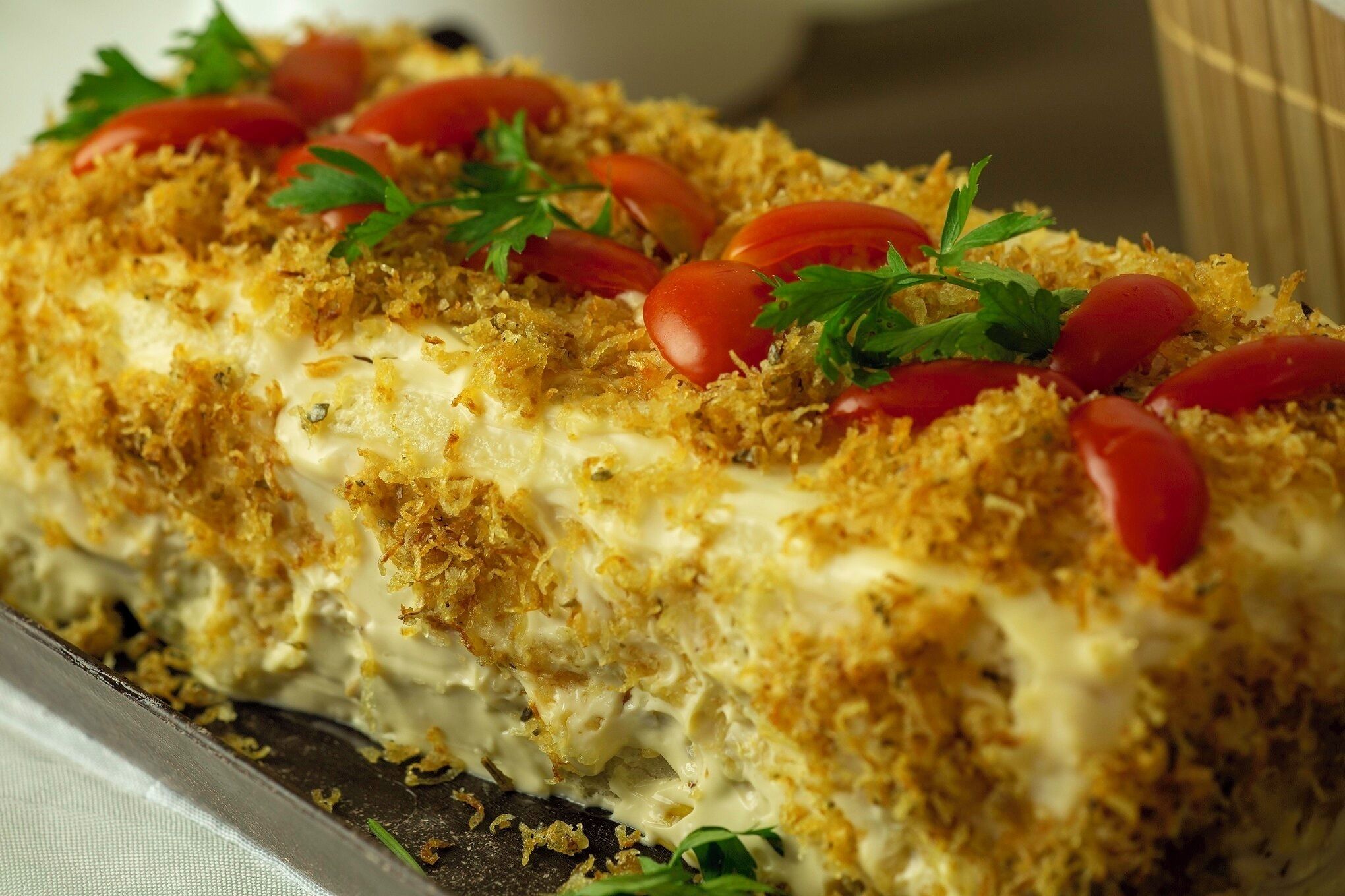 A layered dish with a golden-brown crust, garnished with cherry tomatoes and parsley.