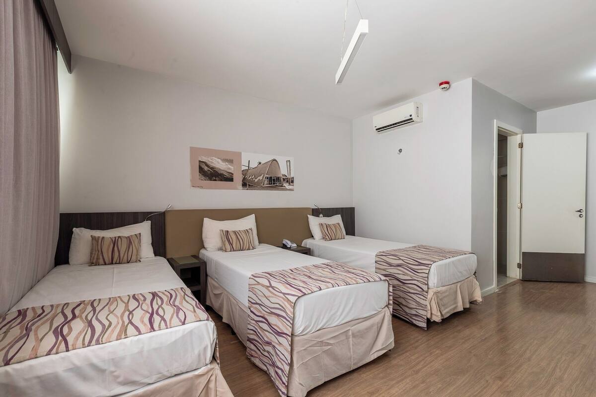 Ein Hotelzimmer mit drei Einzelbetten, einem Nachttisch mit Telefon, einer Klimaanlage und einer Tür zu einem anderen Raum.