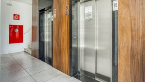 Un área de ascensor moderna con paneles de madera y una puerta de emergencia roja.
