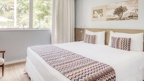 Una habitación de hotel con una cama grande, una ventana con cortinas, una obra de arte en la pared y un cabecero de madera.