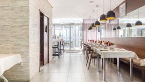 Un comedor moderno con una larga mesa dispuesta para una comida, una pared de ladrillo en un lateral y un vidrio que da a otra habitación.