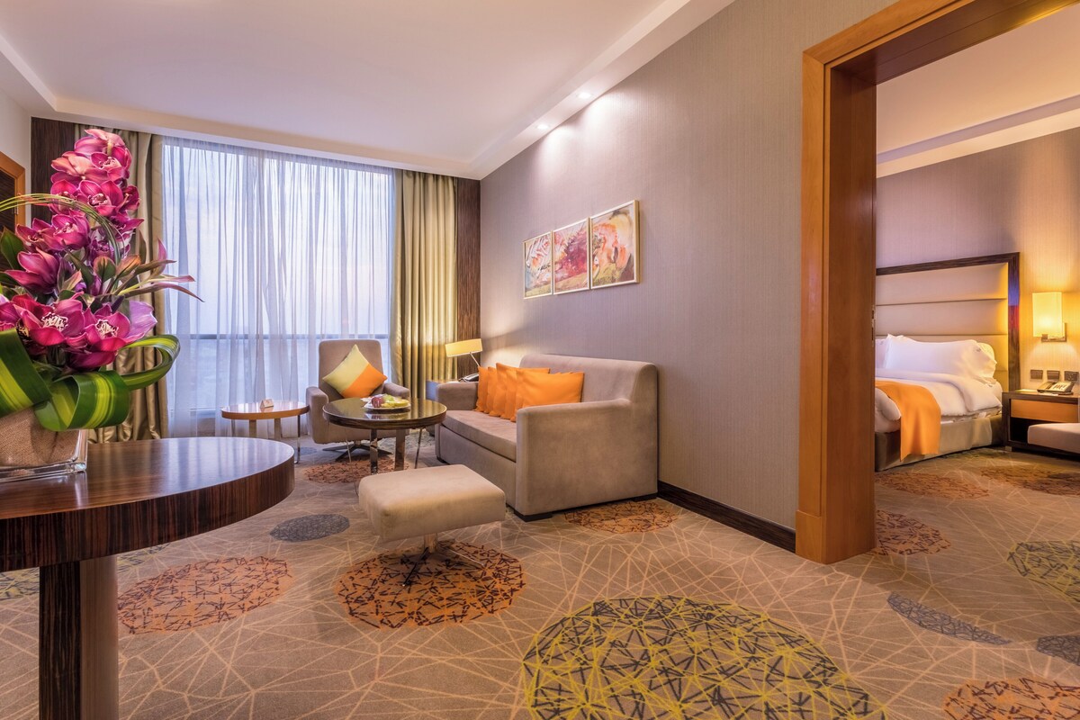 A hotel room with a sofa, armchair, and a dining table.