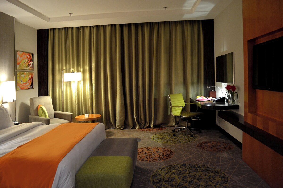 A hotel room with a bed, a desk, a chair, a lamp, and a television.
