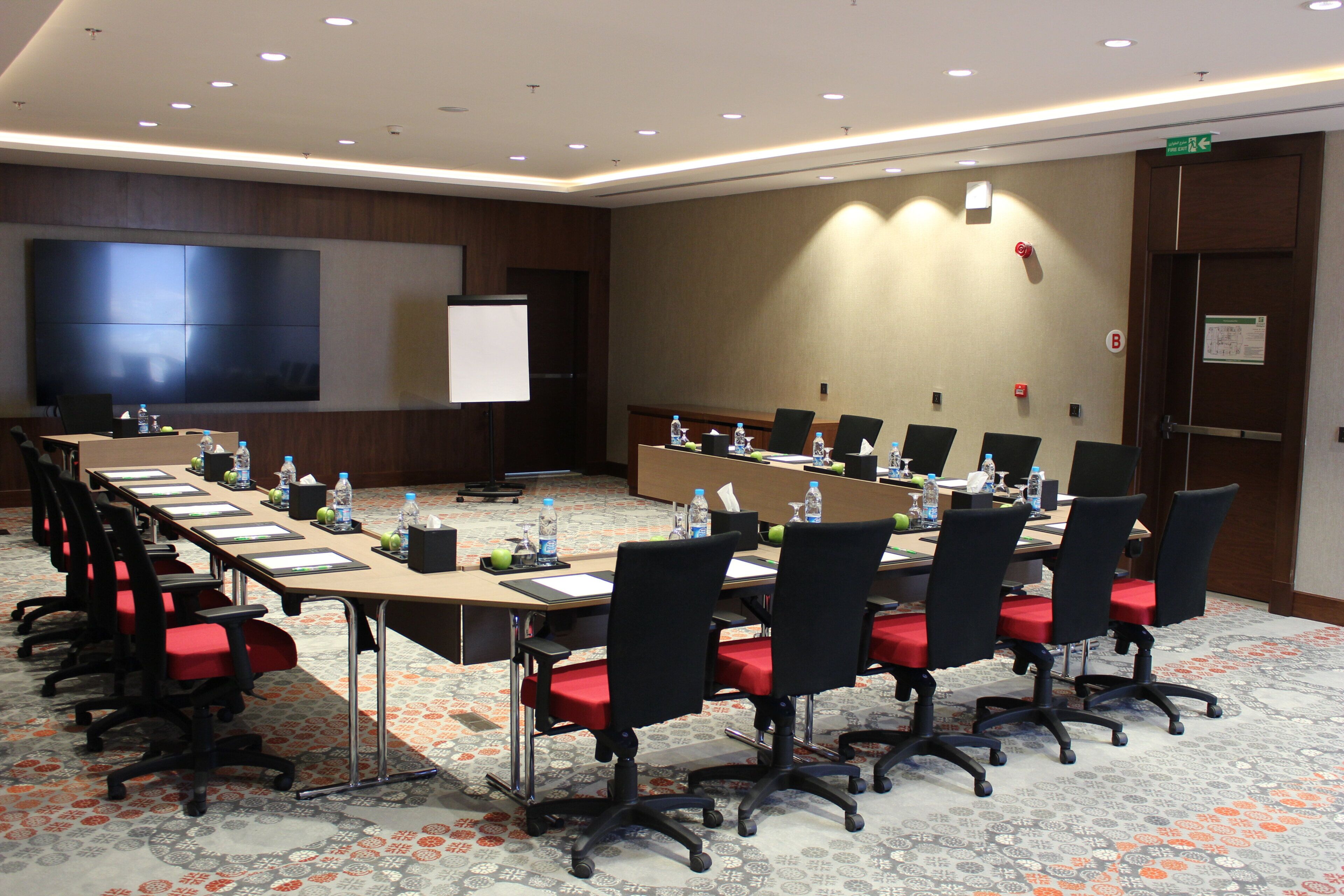 Sala de conferências com uma mesa comprida, cadeiras, tela de projetor e quadro branco.