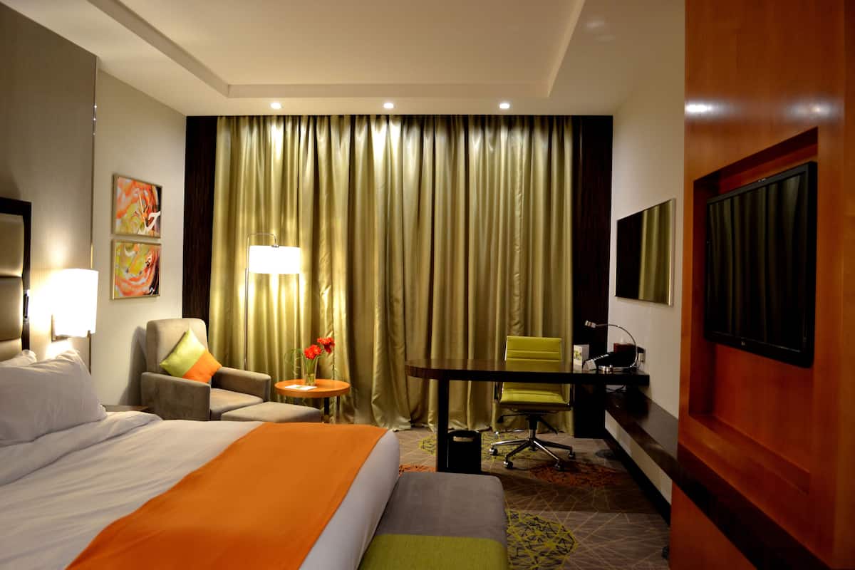A hotel room with a bed, a desk, a chair, a lamp, and a TV.