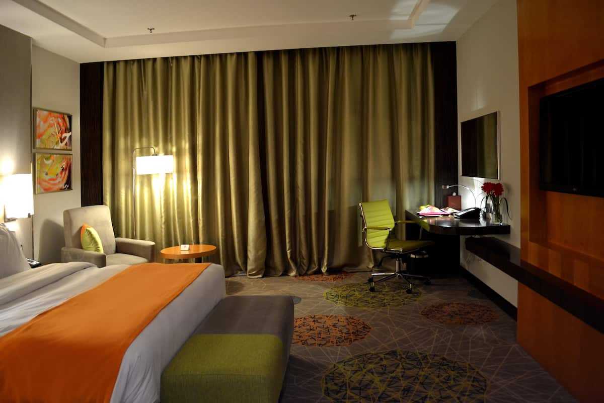 A hotel room with a large bed, a desk, a chair, and a television.
