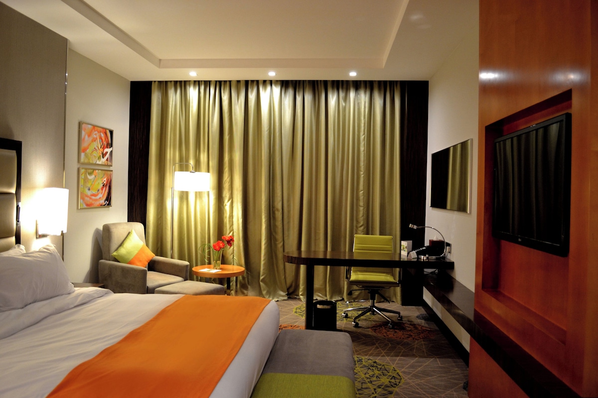 A hotel room with a bed, a desk, a chair, a lamp, a TV, and a curtain.