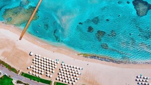 An aerial view of a beach with a pier extending into turquoise waters, a row of sun umbrellas, and a sandy beach area. - Baron Palace Sahl Hasheesh (Sahl Hasheeh)