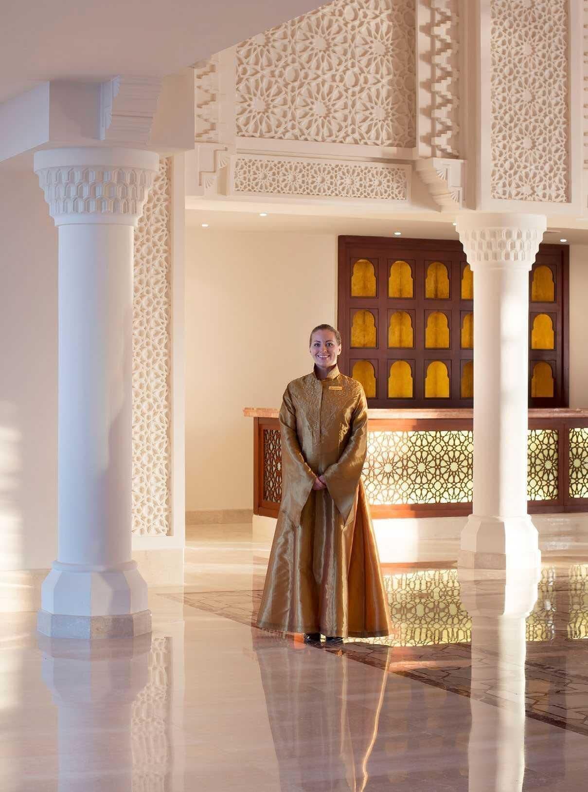 Una persona vestida con traje tradicional en una habitación con columnas blancas ornamentadas y decoraciones elaboradas en las paredes.