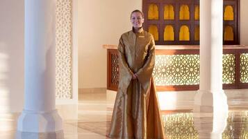 Una persona vestida con traje tradicional en una habitación con columnas blancas ornamentadas y decoraciones elaboradas en las paredes.