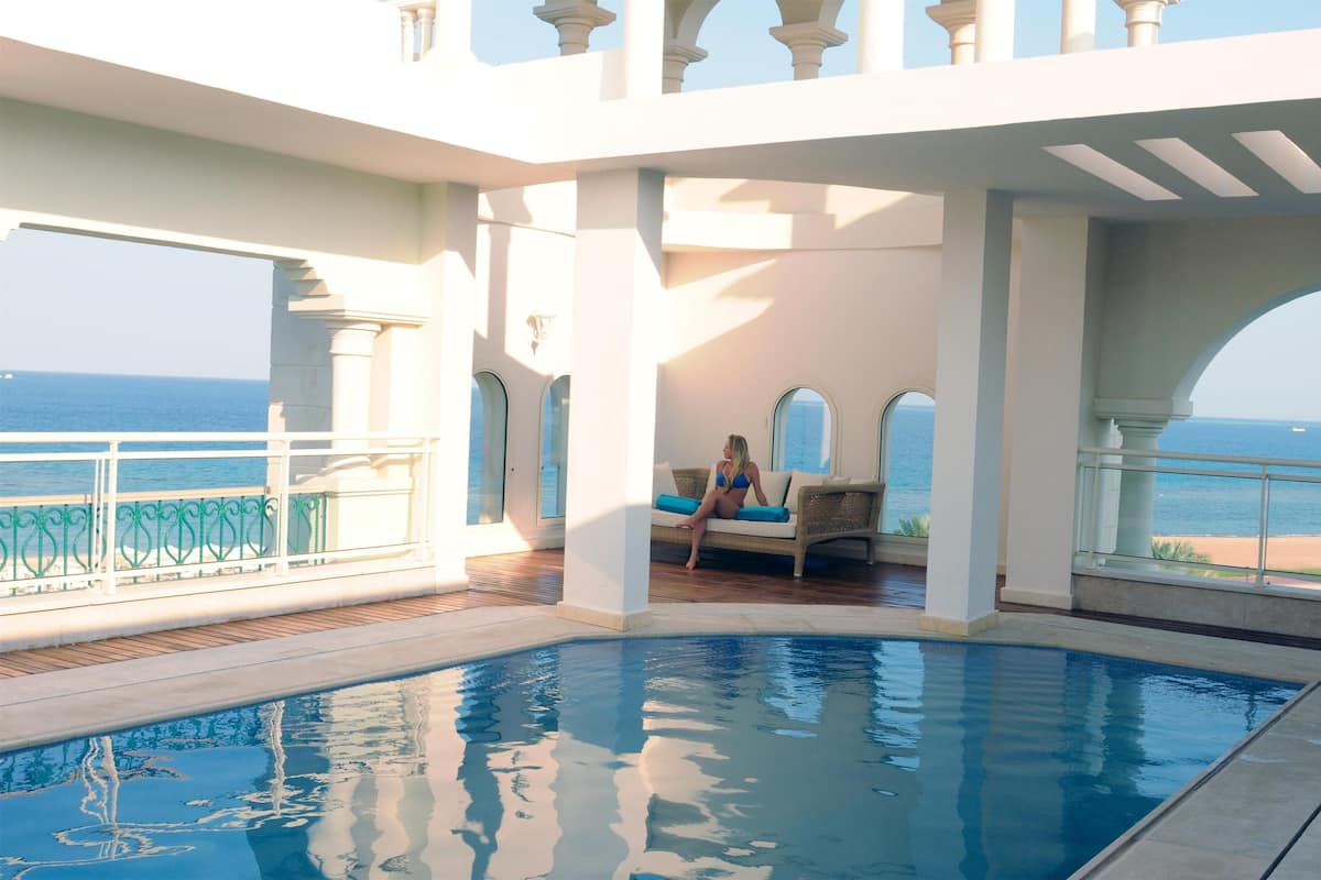 A pool area with a view of the ocean, a lounge chair, and a glass balustrade.