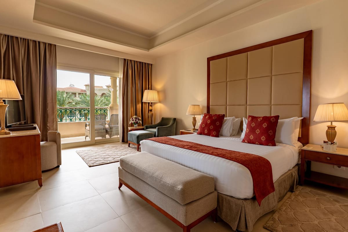 A hotel room with a large bed, a sofa, a TV, and a balcony with a view.