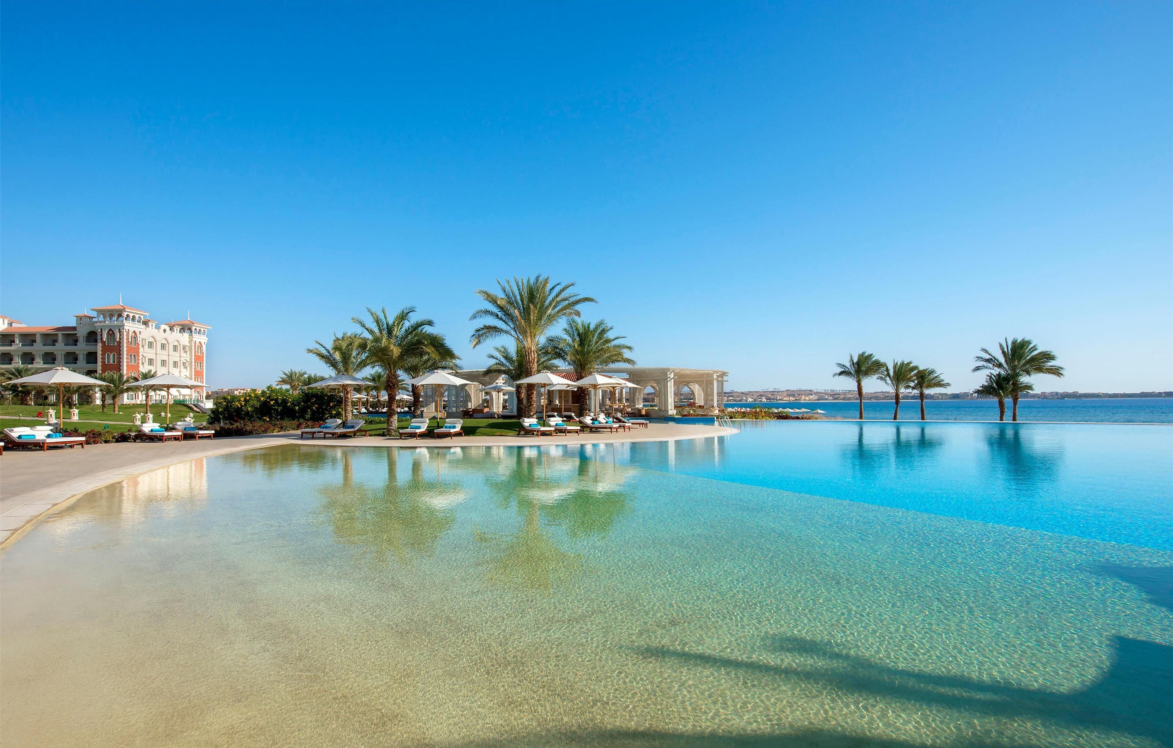 Una piscina di resort con acqua cristallina, palme e un edificio con numerosi balconi.