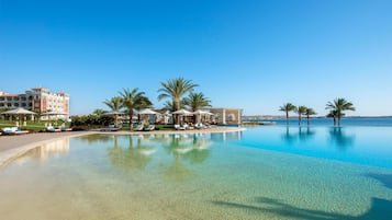 Una piscina di resort con acqua cristallina, palme e un edificio con numerosi balconi.