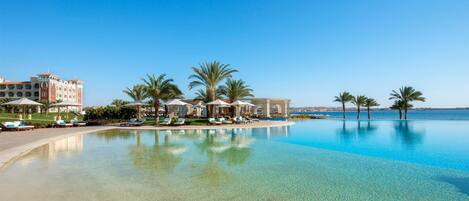 A resort pool with clear water, palm trees, and a building with multiple balconies.