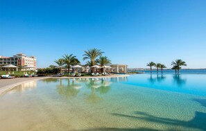 A resort pool with clear water, palm trees, and a building with multiple balconies.
