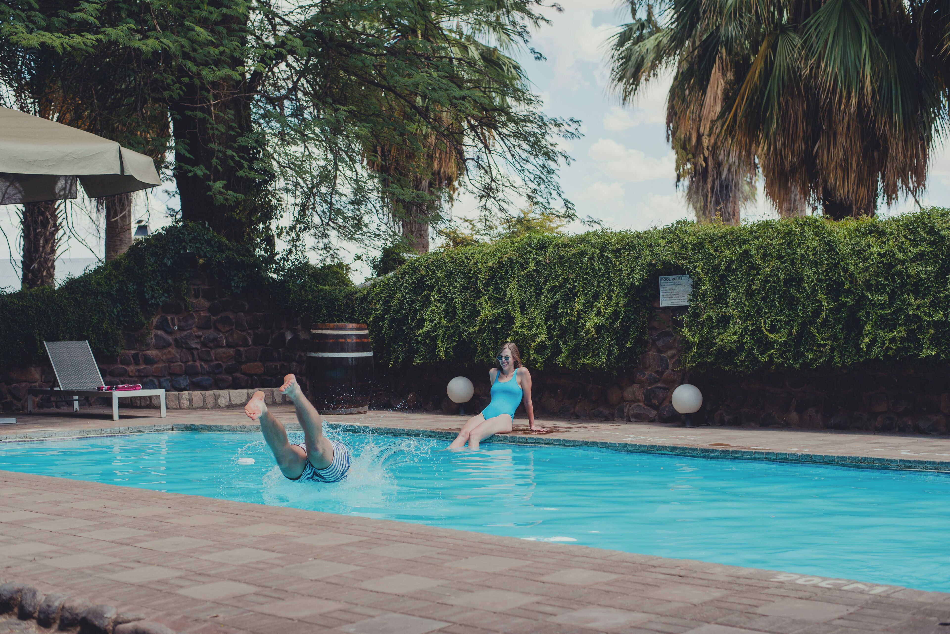 A swimming pool with a person diving and another sitting by the pool.