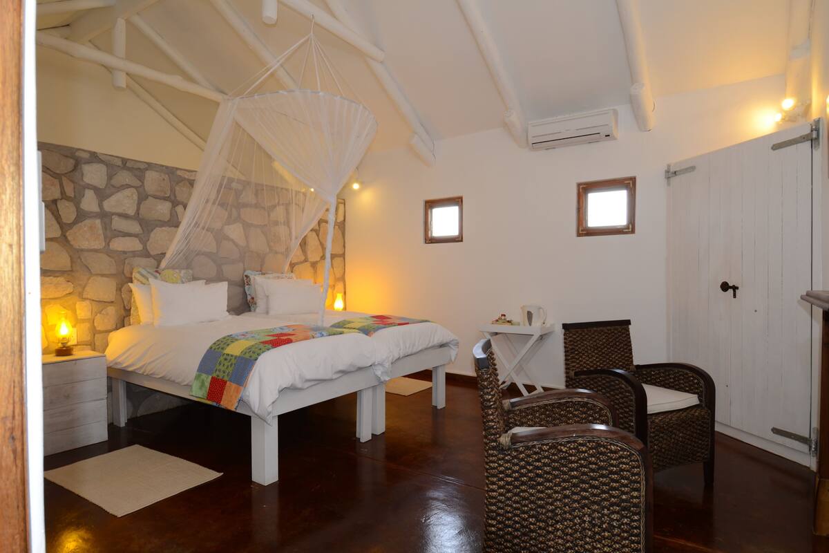 Une chambre à coucher avec un lit, une table de chevet, une chaise et un mur en pierre.