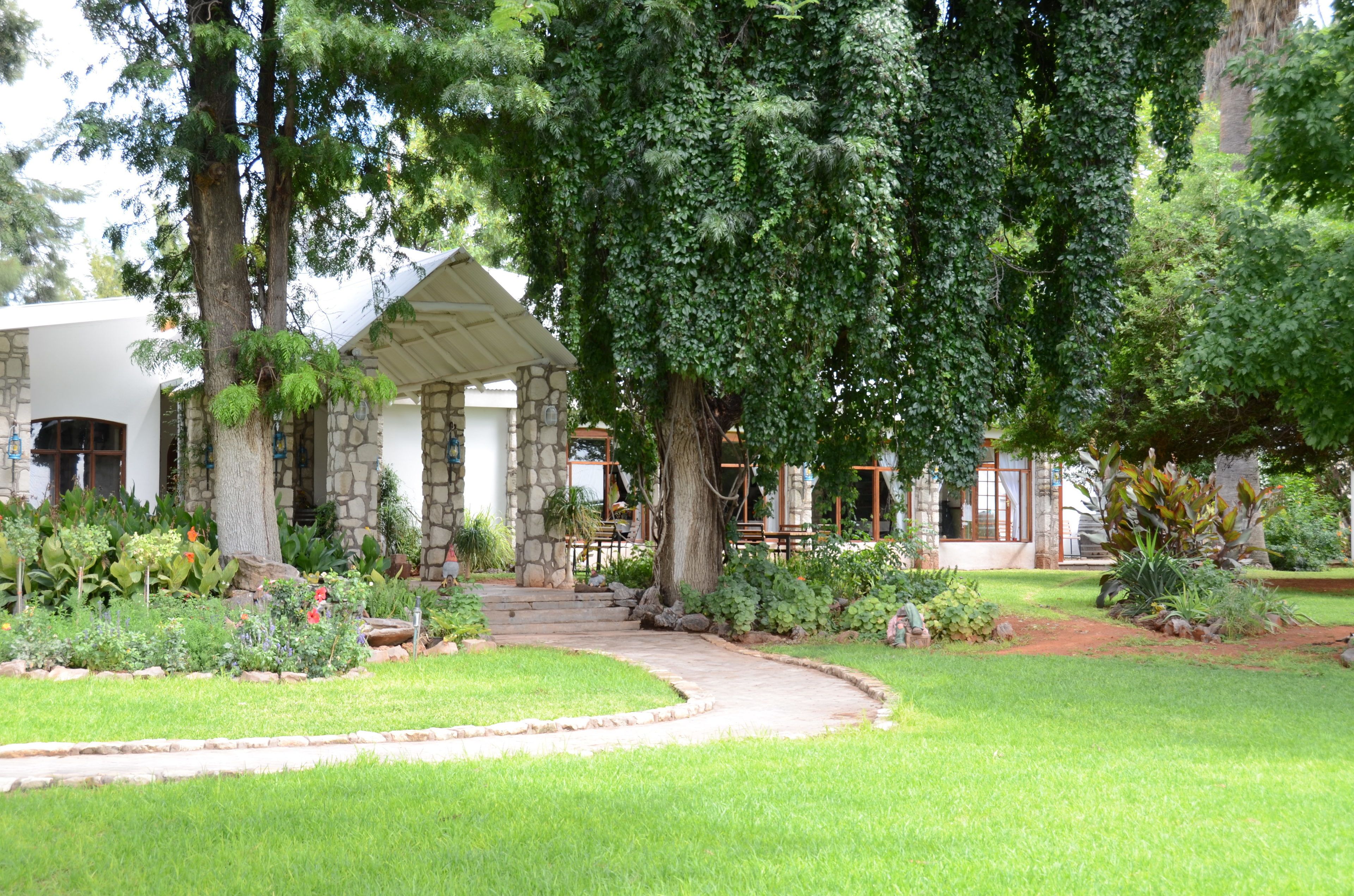 A stone building with a covered patio, surrounded by lush greenery and a well-maintained garden.
