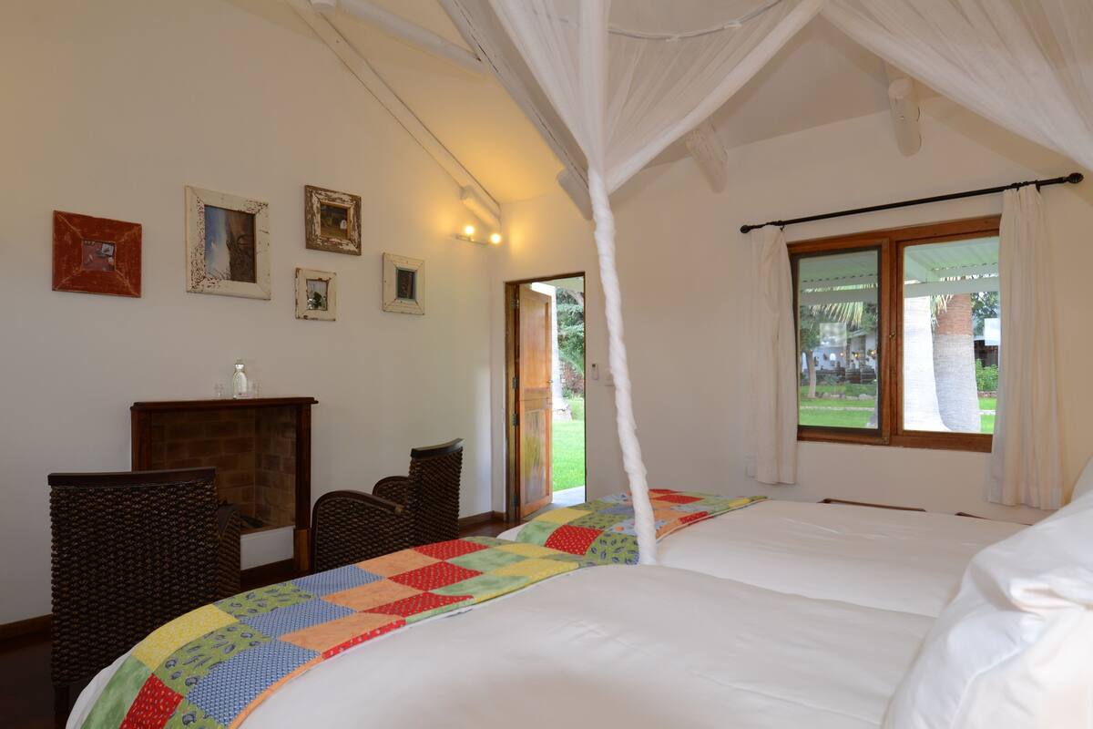 Une chambre à coucher avec un lit, une chaise, une petite table et une fenêtre avec des rideaux.