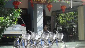 A row of bicycles parked in front of a building with a sign above them. - Homestay Countryside (Da Nang)