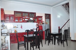 Une cuisine avec des meubles de rangement rouges, une table à manger avec des chaises, et une personne en train de cuisiner.