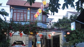 A building with a red tiled roof, a parked car, and a dog in the foreground. - Homestay Countryside (Da Nang)